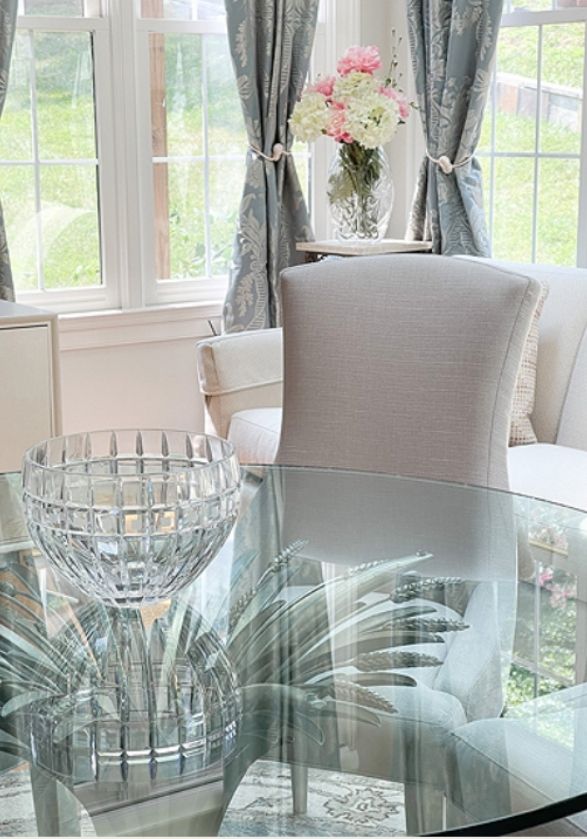 Bright, airy dining area with sheer blue and white patterned curtains and a floral arrangement by a sunny window by statement design concepts